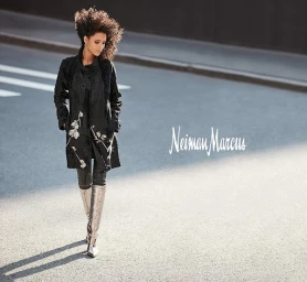 Woman with voluminous dark curly hair wearing an embroidered black coat and tall silver boots walking on an asphalt street
