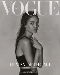 Joan Smalls posing for a Vogue Greece magazine cover in a black sleeveless top against a plain grey background
