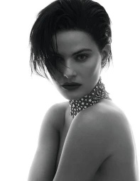 Portrait of a woman with dark slicked-back hair wearing a heavily embellished choker necklace against a bright white background
