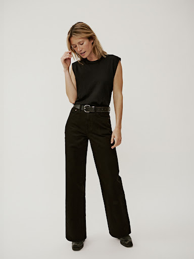 Model wearing a black sleeveless top and black trousers with a leather belt against a white background