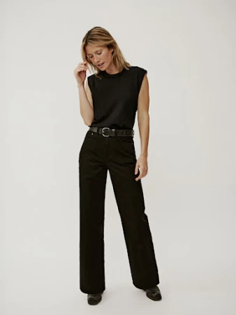 Model wearing a black sleeveless top and black trousers with a leather belt against a white background