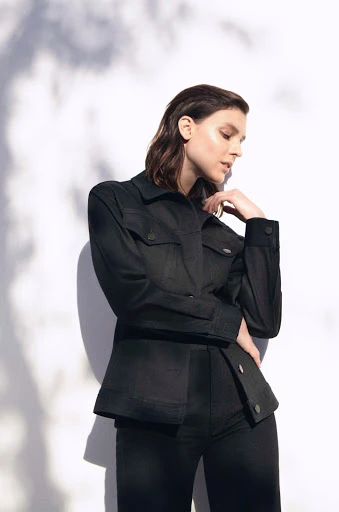 Portrait of a young adult female fashion model in black jacket and pants posing indoors with shadows. Fashion, beauty, studio lighting.