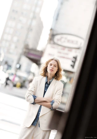 Woman in a light blazer and denim shirt with arms crossed standing on a city street