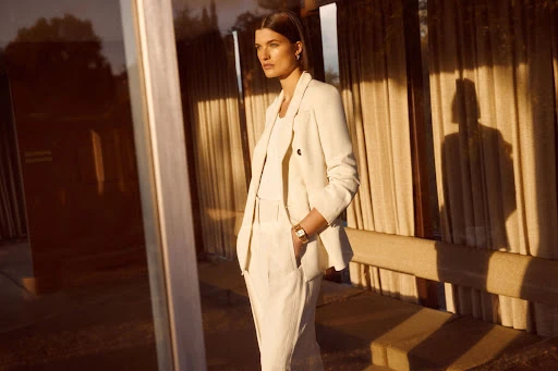 Adult woman in a cream-colored pantsuit poses outdoors with golden sunlight and long shadows, exuding elegance and style in golden hour.