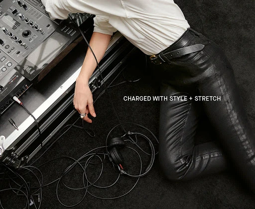 Person in black leather pants poses near audio equipment. High-angle shot shows fashion clothing, hand with ring, and DJ gear.