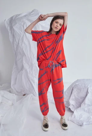 Model wearing red patterned t-shirt and matching sweatpants standing against a crumpled white paper backdrop.