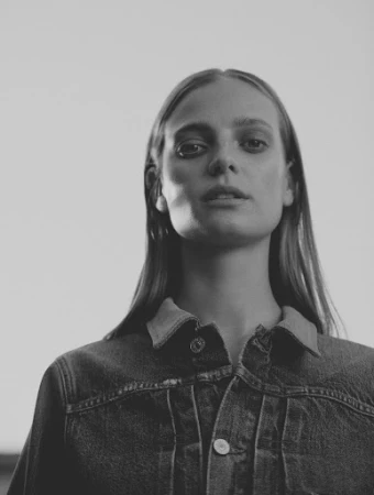 Monochrome portrait of a woman wearing a denim jacket shot from a low angle against a plain light background