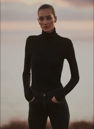 Woman wearing a black turtleneck and dark jeans standing outdoors against an overcast horizon, styled by Annina Mislin.