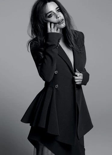 Black and white portrait of a woman in a stylish dark jacket with an asymmetrical hem, posing against a neutral grey background.