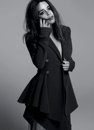 Black and white portrait of a woman in a stylish dark jacket with an asymmetrical hem, posing against a neutral grey background.