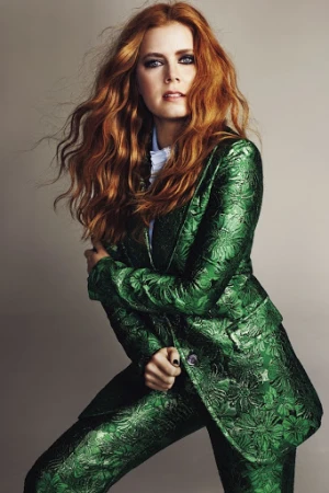 Amy Adams poses in a vibrant green floral suit with stylish wavy red hair against a neutral backdrop in a fashion studio shot.