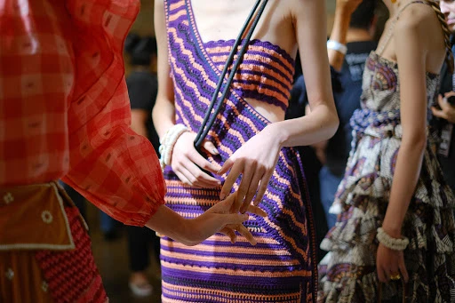 Three women in dresses pose in an indoor setting. One woman wears red gingham while the others wear patterned dresses.