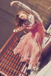 Red-haired model in a pink tulle dress posing on an outdoor metal fire escape staircase styled by April Hughes