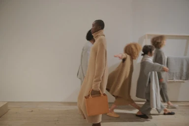 Group of models walking in a neutral interior space styled by April Hughes, featuring knitwear and a leather handbag