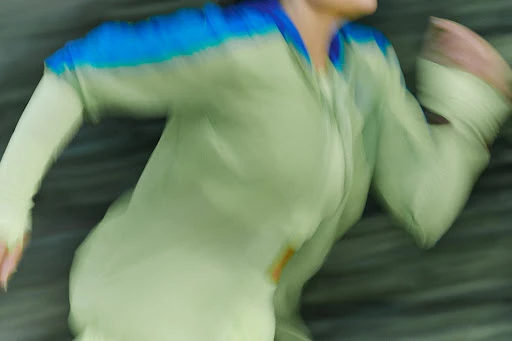 Motion blur of a figure in a light green and blue top, with the colors and shapes suggesting running or athletic activity.