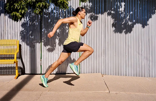 Athletic man powerfully sprints outdoors on a paved surface, showcasing fitness and determination against a metal fence backdrop.