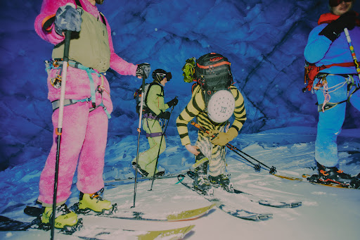 Group of four people in winter mountaineering gear skiing through a snow-covered cave featuring blue ice formations and rugged terrain.