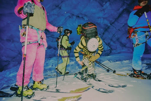 Group of four people in winter mountaineering gear skiing through a snow-covered cave featuring blue ice formations and rugged terrain.