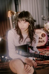 Young woman holding an electric guitar in a rehearsal space styled by Charlotte Patterson
