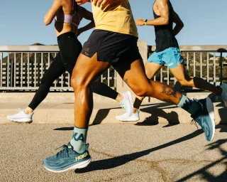 Group of runners in athletic wear running together outdoors on a sunny bridge with long shadows