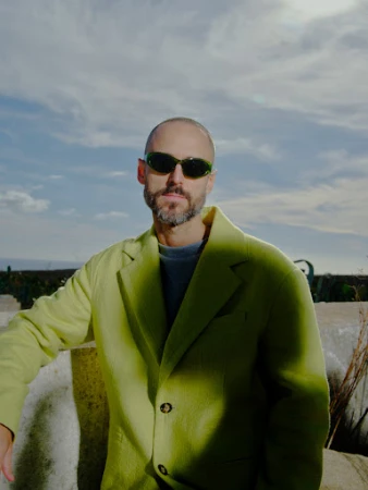 Man wearing lime green blazer and dark sunglasses outdoors under a cloudy sky styled by Charlotte Patterson
