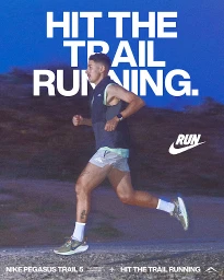 Man running outdoors on a trail wearing grey shorts, white socks, and a dark vest against a hilly background at dusk.
