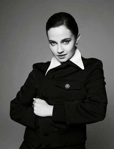 Black-and-white portrait of a woman with dark hair and fair skin, wearing a black jacket and a white collar, posing in a photo studio.