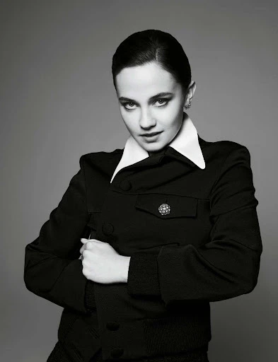 Black-and-white portrait of a woman with dark hair and fair skin, wearing a black jacket and a white collar, posing in a photo studio.