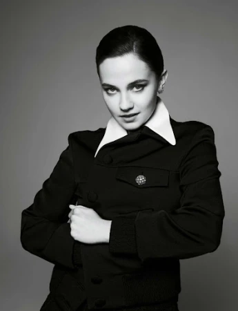 Black-and-white portrait of a woman with dark hair and fair skin, wearing a black jacket and a white collar, posing in a photo studio.