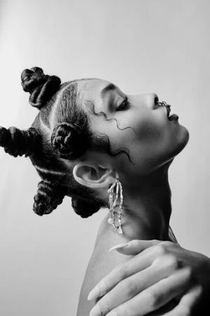Black and white profile portrait of a woman with braided hair knots and dangling statement earrings against a light background.
