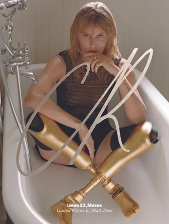 Adult woman with prosthetic legs poses in a bathtub for magazine cover. She wears a dark top and sits confidently, looking directly at the camera.