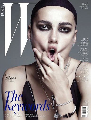 W Korea magazine cover featuring a woman with dramatic eye makeup, jewelry, open mouth, and hand on her face, against a grey backdrop.