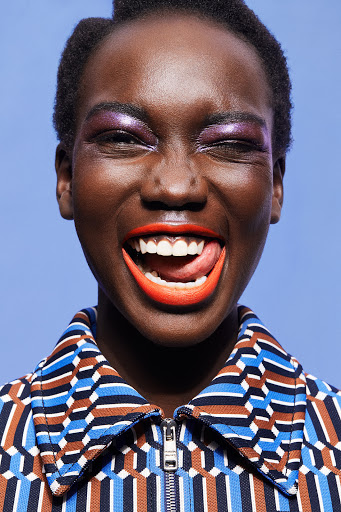 Close-up portrait of a Black female model with bright make-up and open mouth shows tongue. Blue background. Fashion and beauty concept.