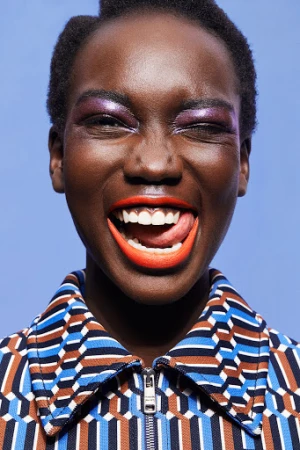 Close-up portrait of a Black female model with bright make-up and open mouth shows tongue. Blue background. Fashion and beauty concept.