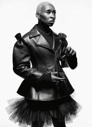 Black and white portrait of a person with short hair wearing a leather jacket and dark layered skirt against a white background