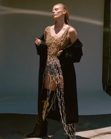 Model with slicked-back hair wearing a textured beaded top and black coat styled by Daniel Edley against a seamless backdrop