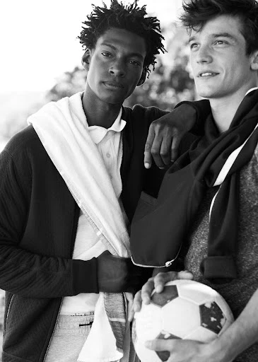 Two men outdoors in black and white, one holding a soccer ball, both with casual athletic wear, enjoying a sunny day in a natural setting.