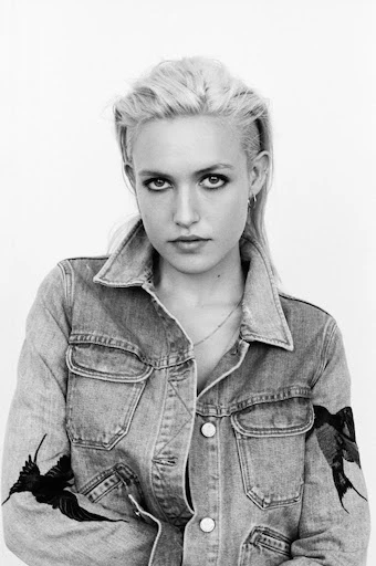 Black and white portrait of a blonde adult female wearing a denim jacket with a bird design on the sleeves against a white background.
