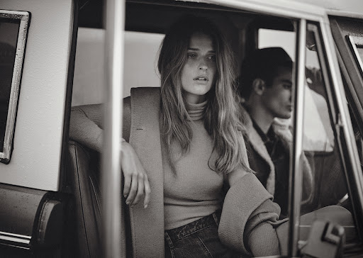 Monochrome fashion portrait of a woman seated in a vintage car with a man in the driver seat