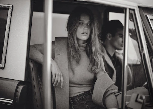 Monochrome fashion portrait of a woman seated in a vintage car with a man in the driver seat
