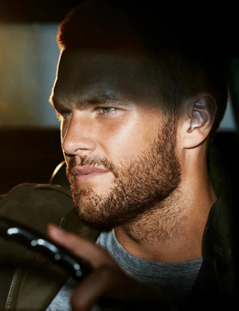 Close-up portrait of a man with a beard driving a vehicle, styled by Deborah Watson