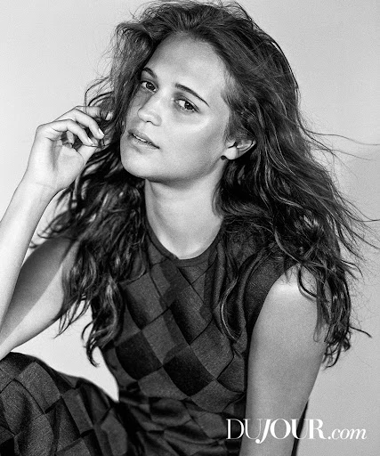 Portrait of a brunette woman in a black and white checkered top with her hand on her head, looking at the camera in a studio.