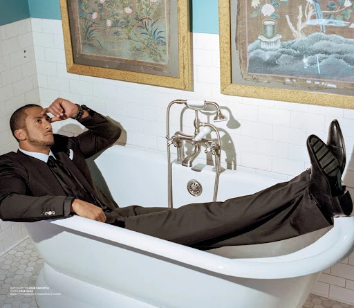 Adult male wearing a suit reclines in a white bathtub with framed artwork on the wall, creating a sophisticated and relaxed atmosphere.