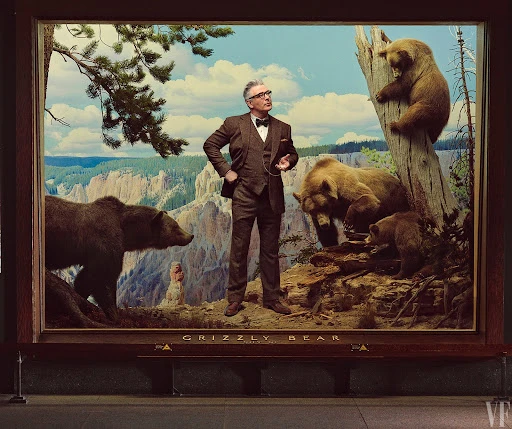 Man in suit stands in front of framed museum display with grizzly bears and a mountain vista as an art installation.