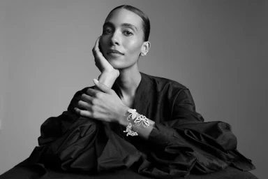 Black and white studio portrait of a woman wearing butterfly jewellery and a dark ruffled top, styled by Deborah Watson.