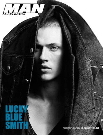 Black and white portrait of Lucky Blue Smith draped in a heavy dark denim jacket against a plain background