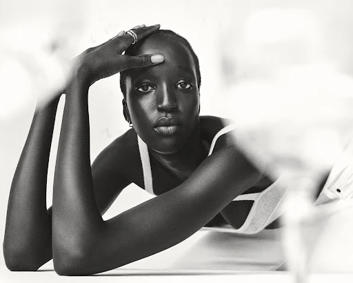 Black woman with short hair posing with hands on head wearing minimalist white strap top in black and white portrait.