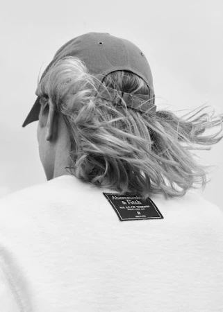 Monochrome portrait of a person from behind wearing a baseball cap and white t-shirt styled by Deborah Watson.