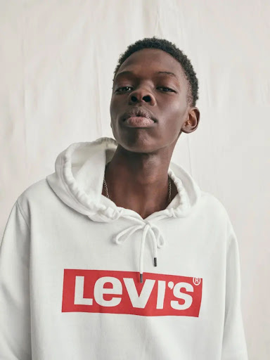 Portrait of an adult Black male wearing a white Levi's hoodie against a neutral backdrop in a studio setting. Fashion photography.