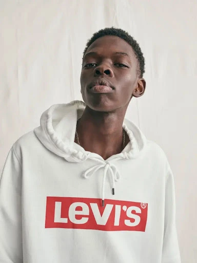 Portrait of an adult Black male wearing a white Levi's hoodie against a neutral backdrop in a studio setting. Fashion photography.